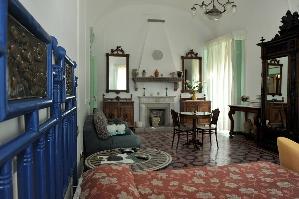 A room with a fireplace, a dining table with chairs, a sofa, and a blue railing with artwork.
