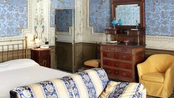 Una habitación con una cama grande, un sofá, un aparador de madera, un espejo y una araña.