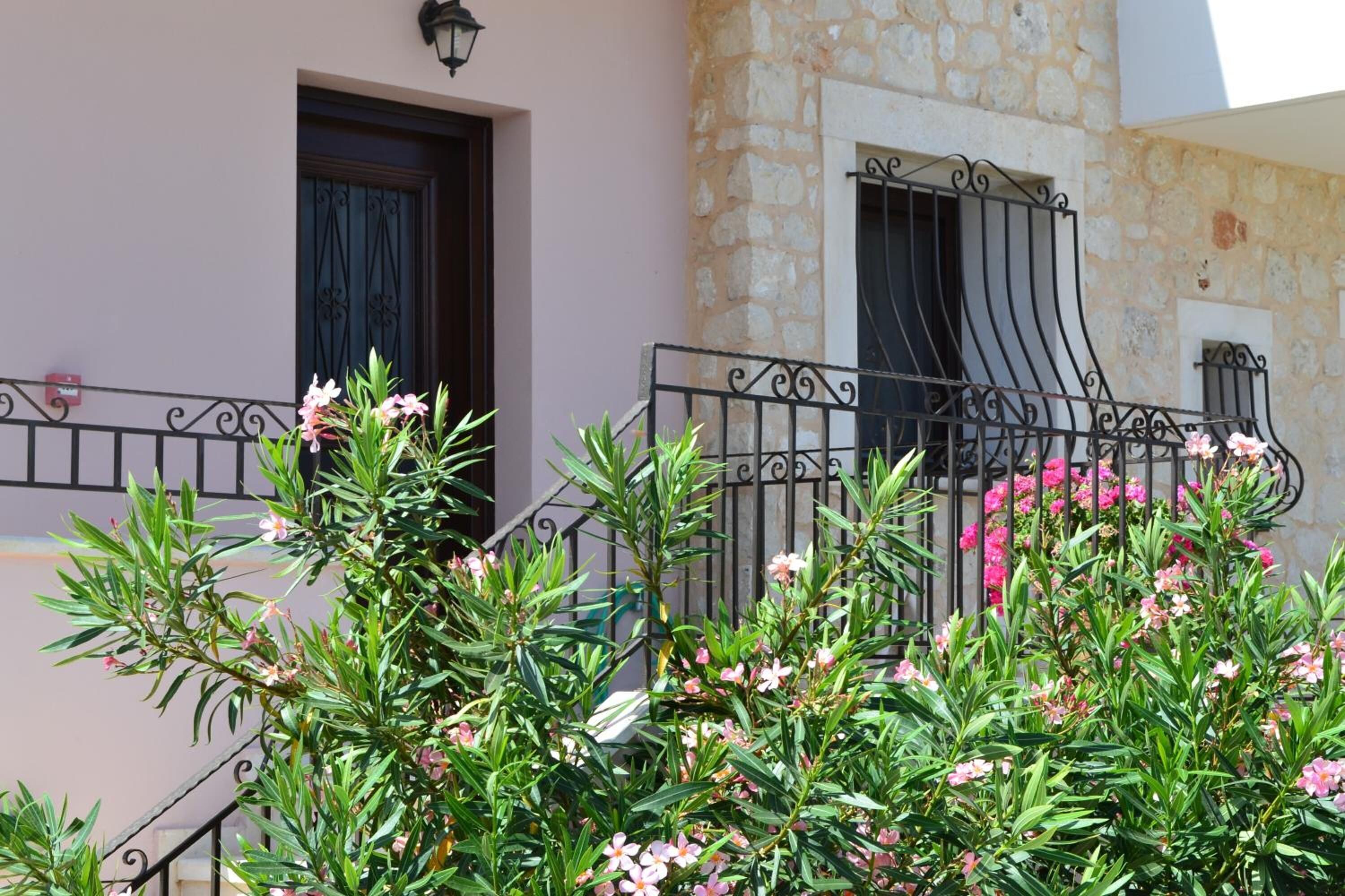 A building with a stone facade, a balcony with wrought iron railings, and flowering plants in the foreground.
