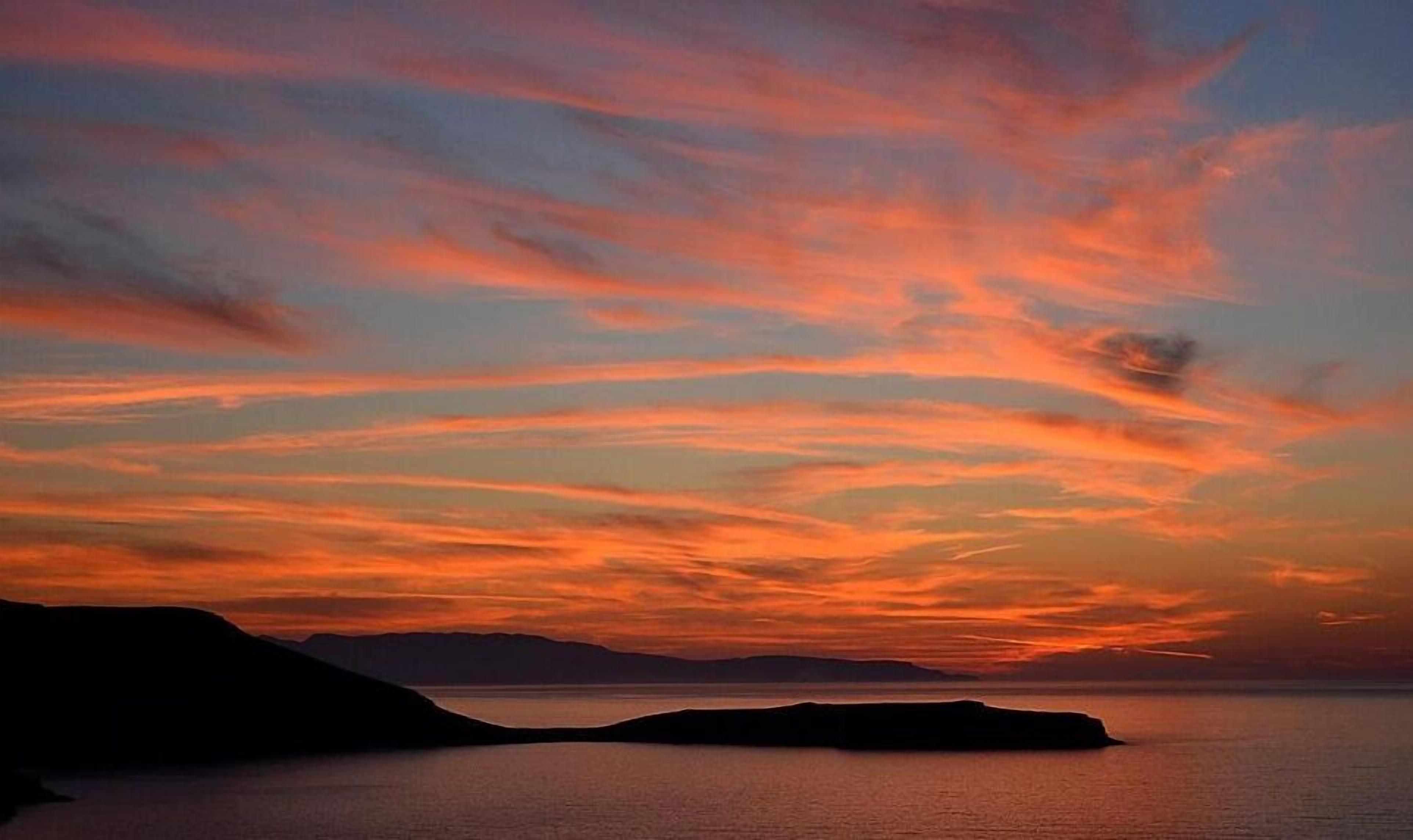 A sunset over a calm sea with distant landforms.