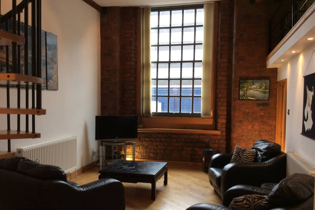 A cozy living room with a fireplace, leather sofas, a flat-screen TV, and a large window with a view of the sea.