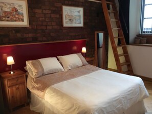 A bedroom with a brick wall, a red headboard, a wooden ladder, and two bedside lamps. - Trafalgar Warehouse Apartments (Liverpool)