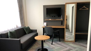 Habitación de hotel con sofá, una mesita redonda, televisor montado en la pared y un escritorio de madera.