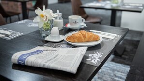 Un desayuno con un croissant, café, leche y un periódico sobre la mesa.