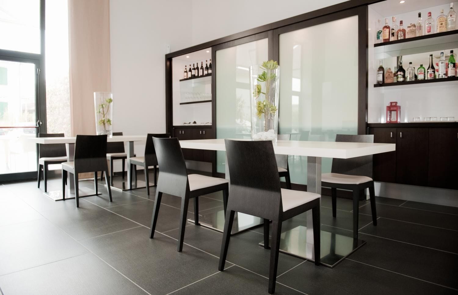 Un espace de restauration moderne avec une cloison en verre, des chaises noires et une table blanche.
