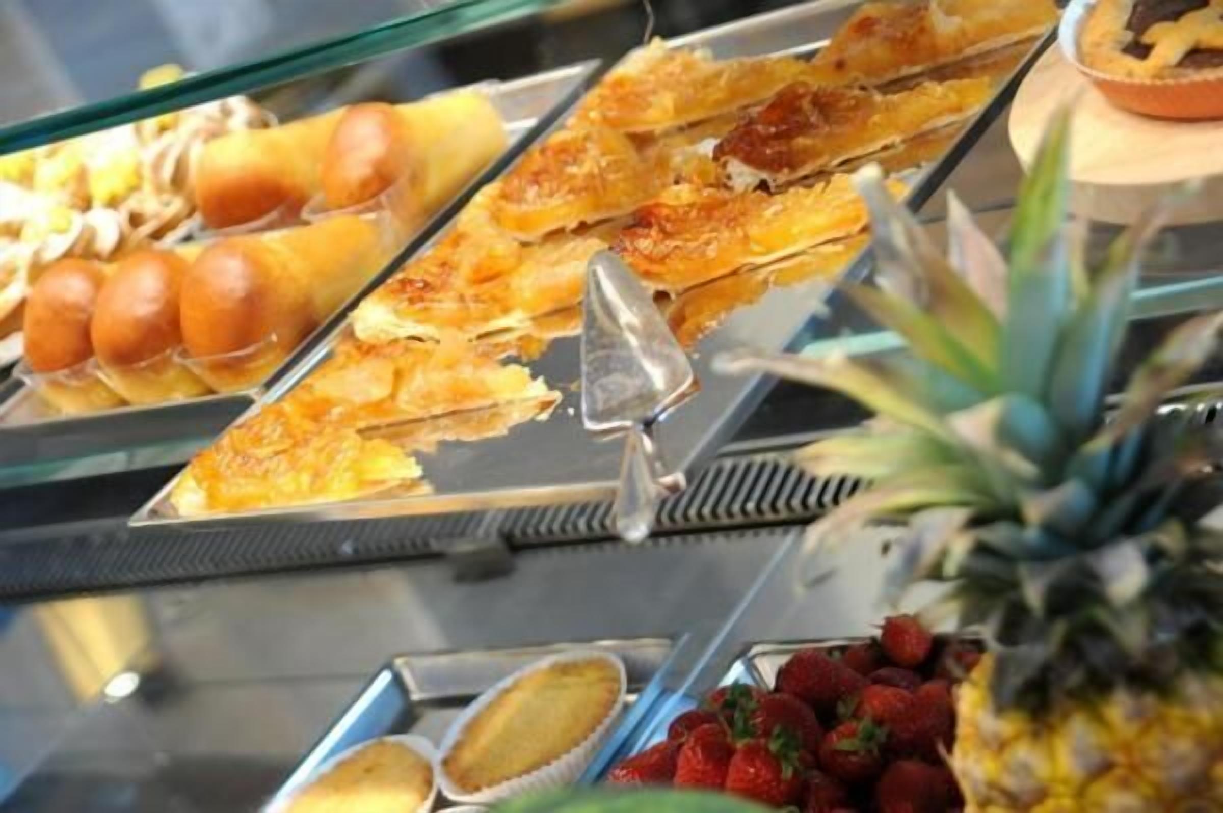 Un bufé con diversas opciones de comida, como tartas, pasteles y frutas, incluyendo fresas y piña.