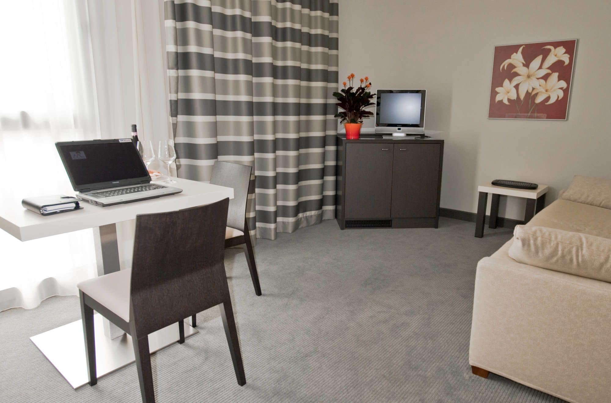 Uma sala moderna com área de jantar, TV de tela plana em um móvel, sofá e escrivaninha com laptop e copos de vinho.