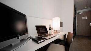 A hotel room with a desk, a laptop, a flat-screen TV, a lamp, and a bottle of wine.