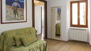 Une pièce avec un canapé vert, une table en verre, un radiateur et une porte donnant sur une autre pièce.