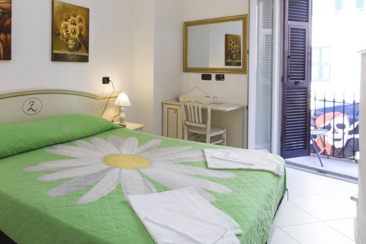 A bedroom with a green bedspread, a nightstand with a lamp, a desk, and a chair.