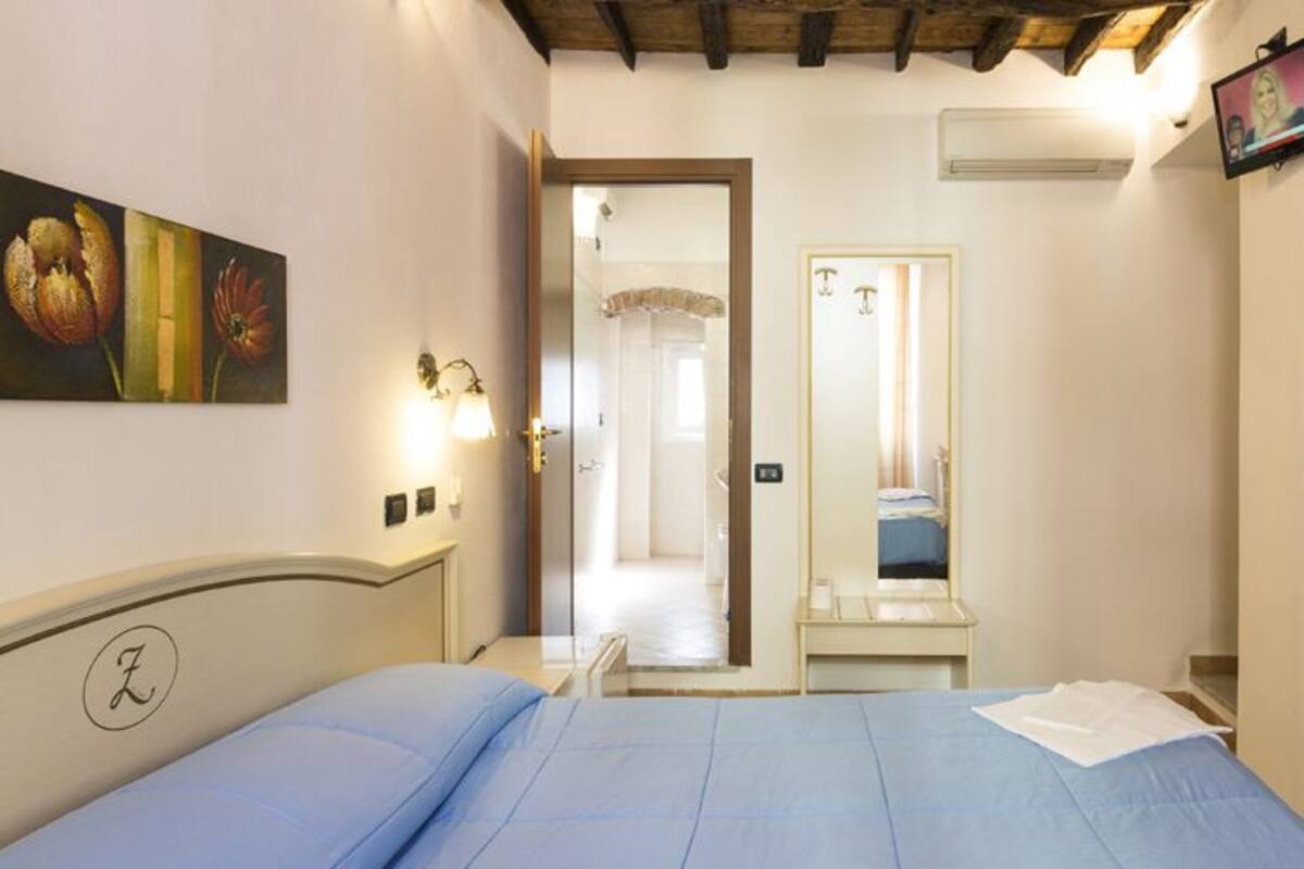A bedroom with a bed, a painting, a mirror, and a stone wall.