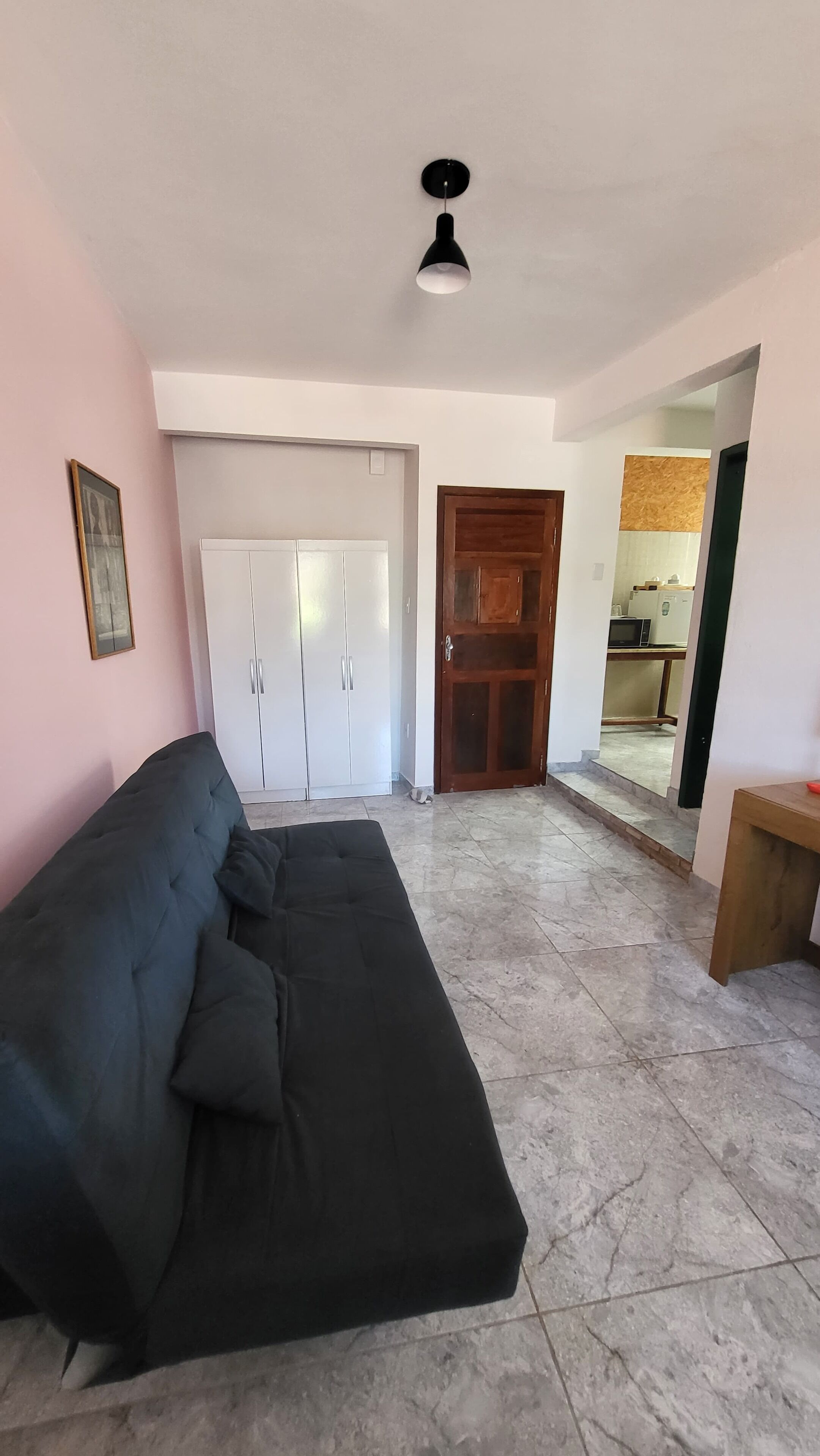 A living room with a black sofa, white wardrobe, and a wooden door leading to a kitchen area.