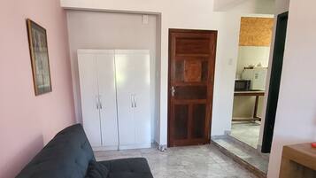 A living room with a black sofa, white wardrobe, and a wooden door leading to a kitchen area.