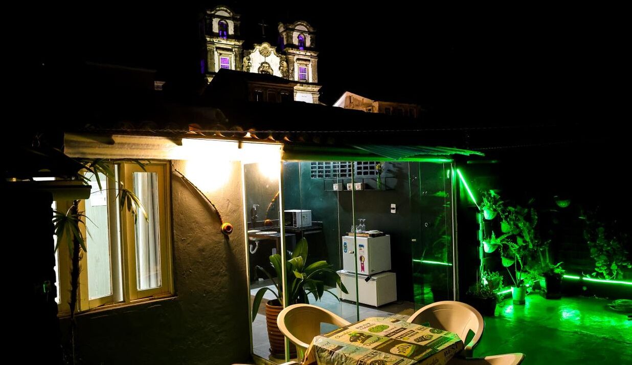A small, enclosed outdoor space with a table and chairs, a refrigerator, and a potted plant.