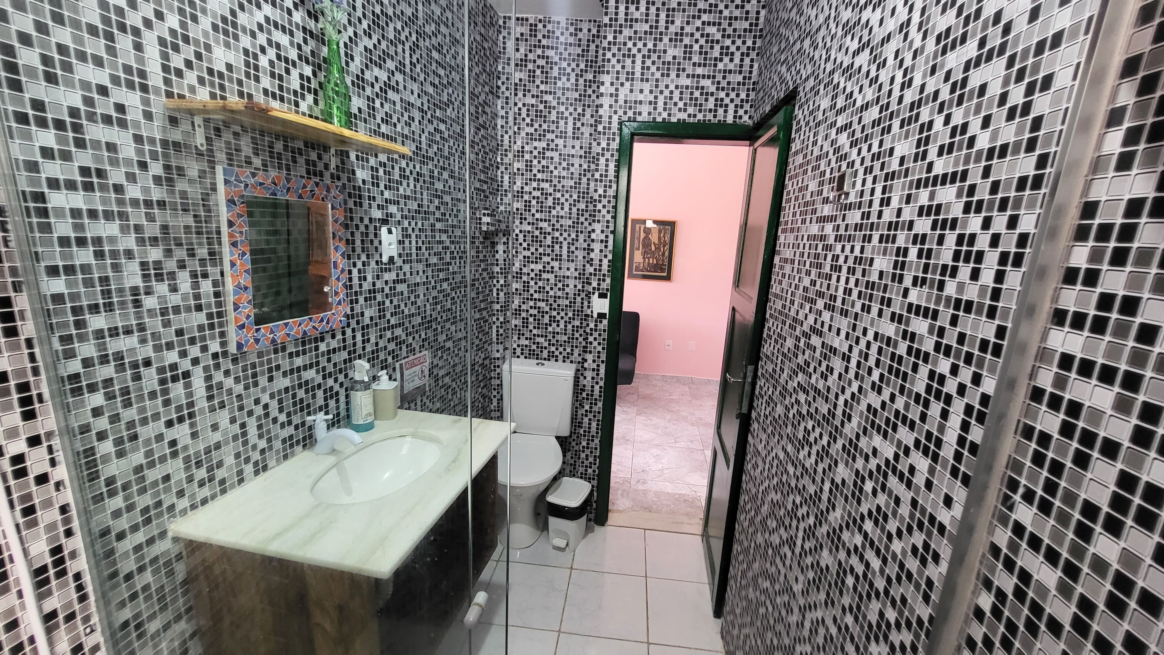 Un bagno con parete rivestita in mosaico piastrellato, lavandino con specchio e water.