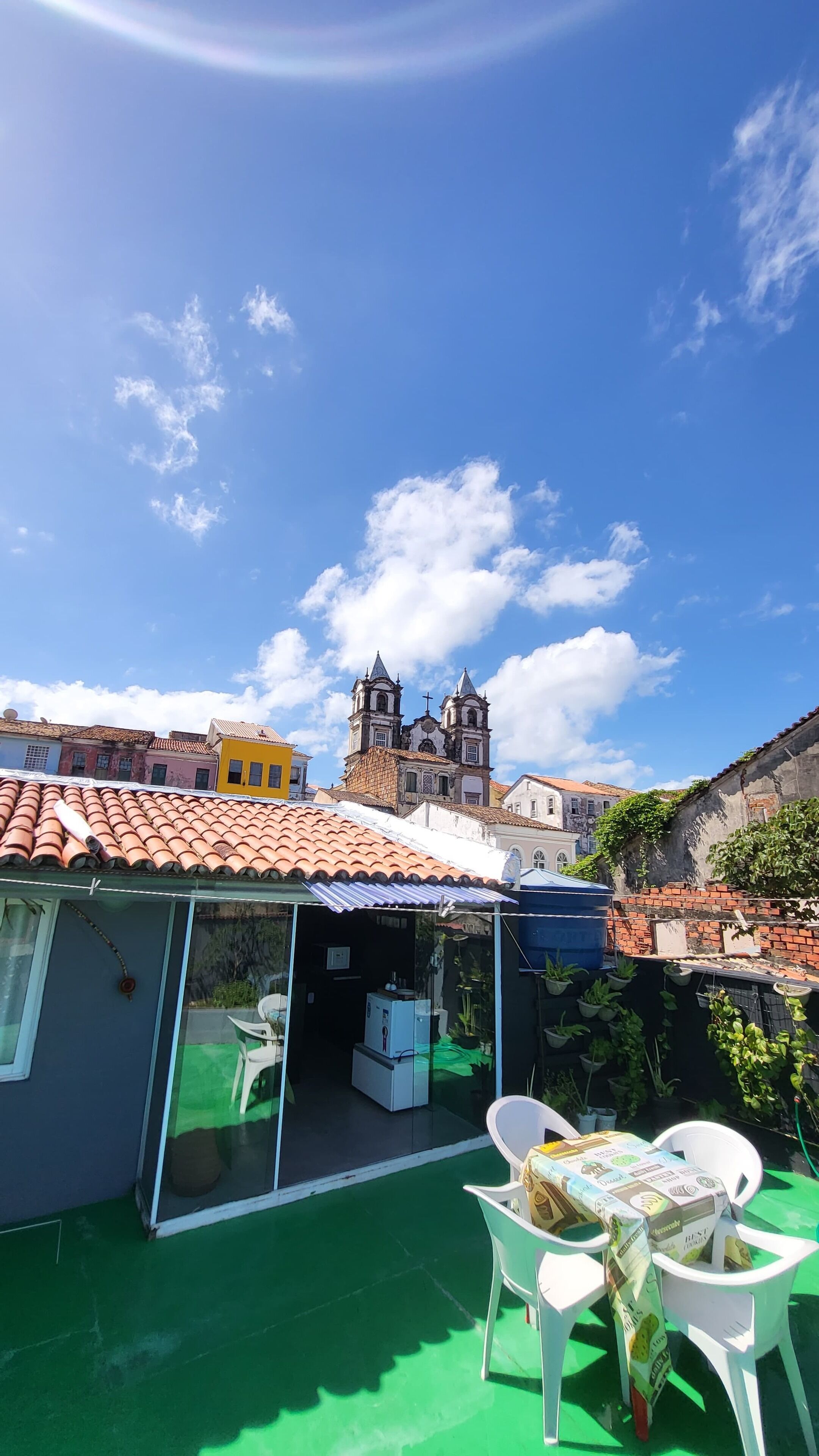 A rooftop patio with a table and chairs, a glass enclosure, and a view of a historic church with two towers.
