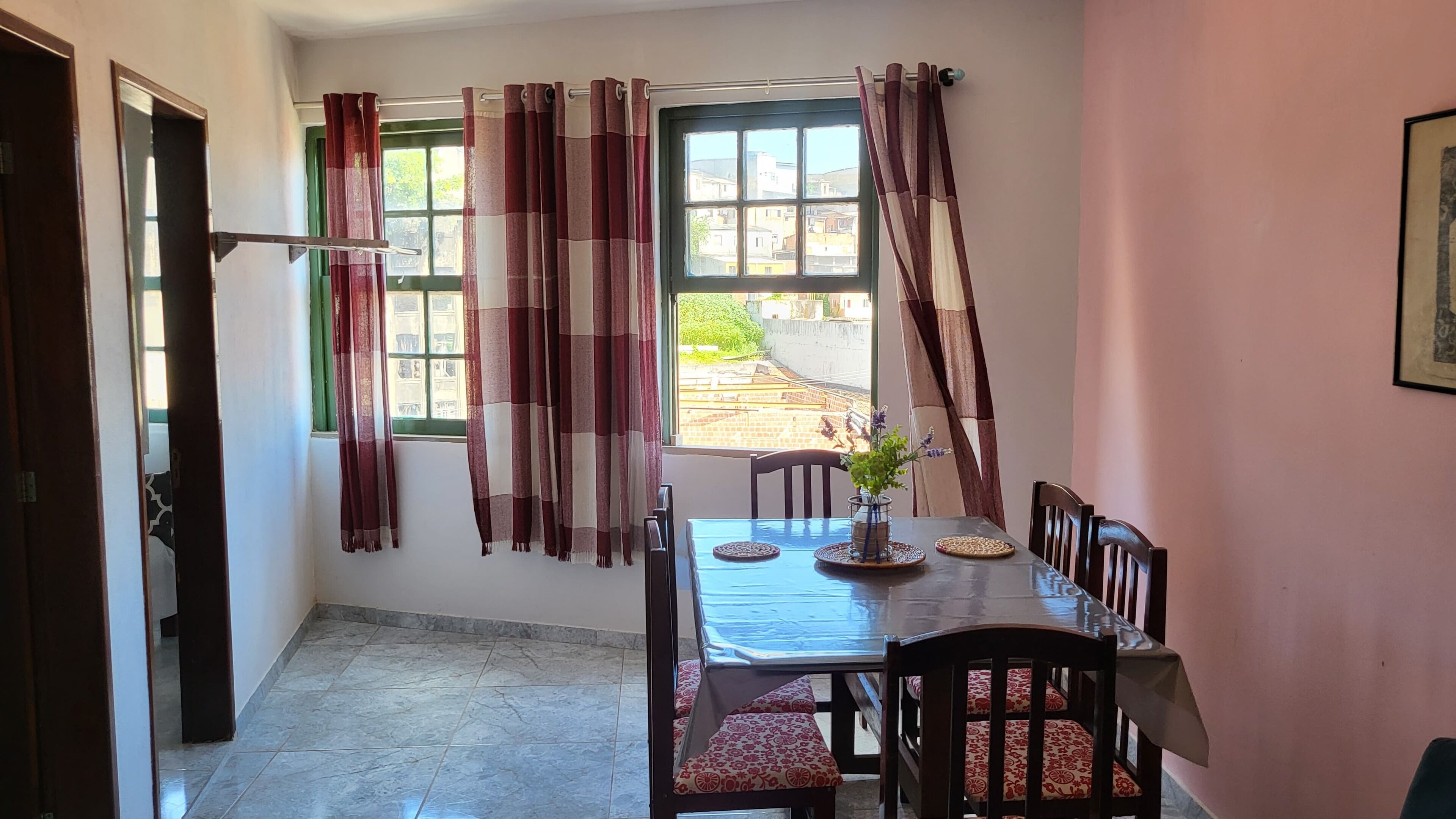 Un comedor con una mesa y sillas, una ventana con cortinas, y vistas a edificios.