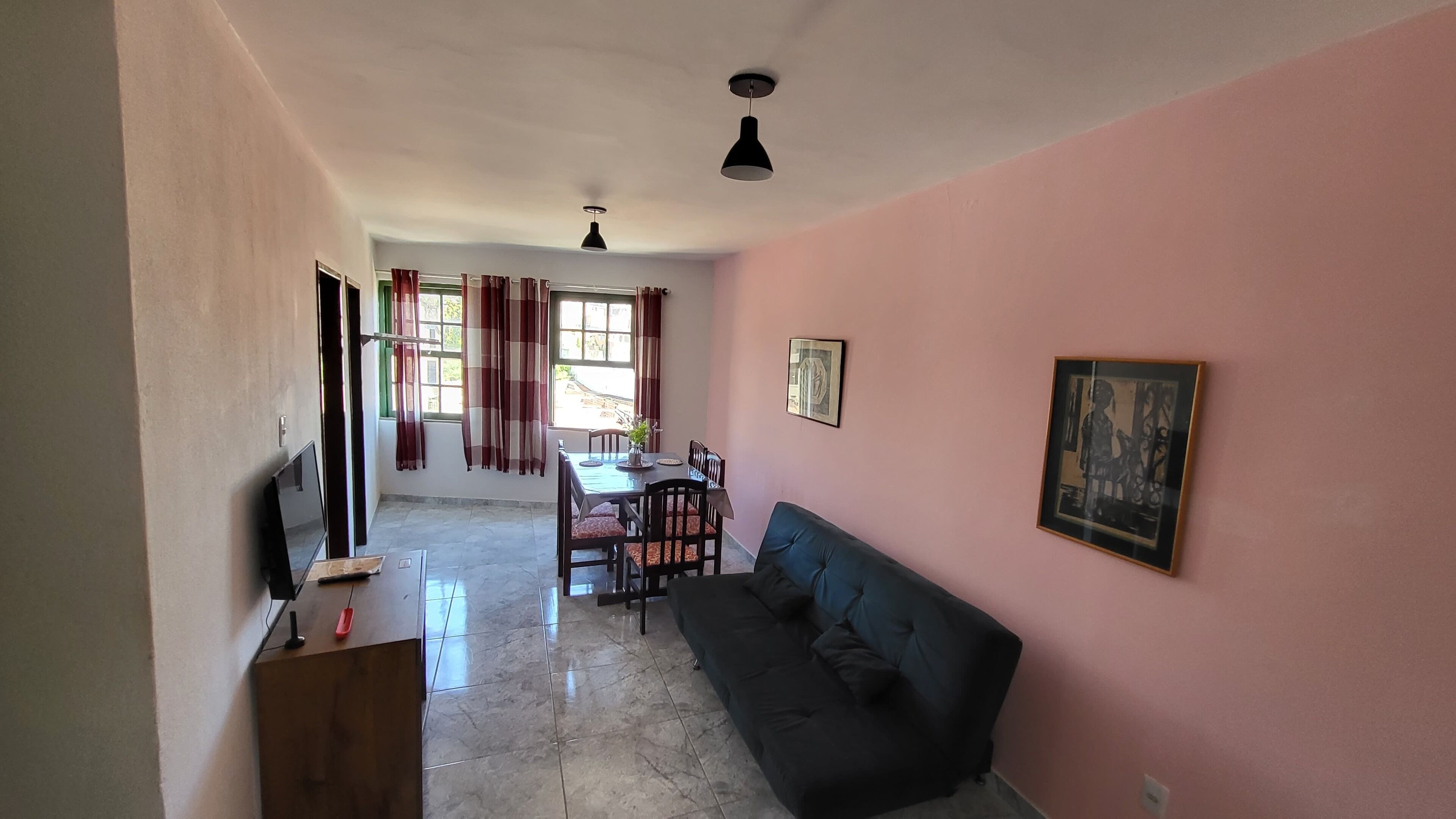 Una sala de estar con sofá, una mesa de comedor con sillas, televisor y una lámpara de techo.