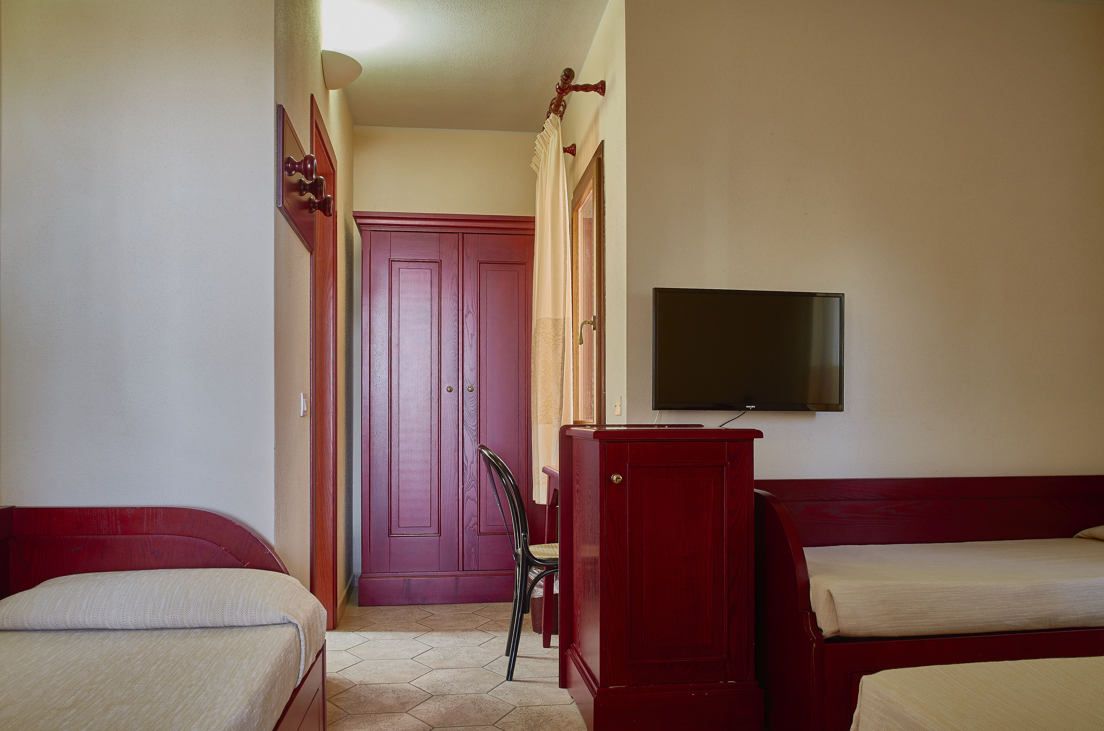 A hotel room with two single beds, a TV mounted on the wall, and a wooden wardrobe.