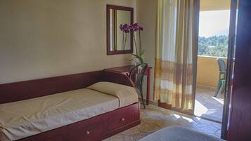 A bedroom with a bed, a nightstand, a mirror, a vase with flowers, and a view of a balcony with a chair.