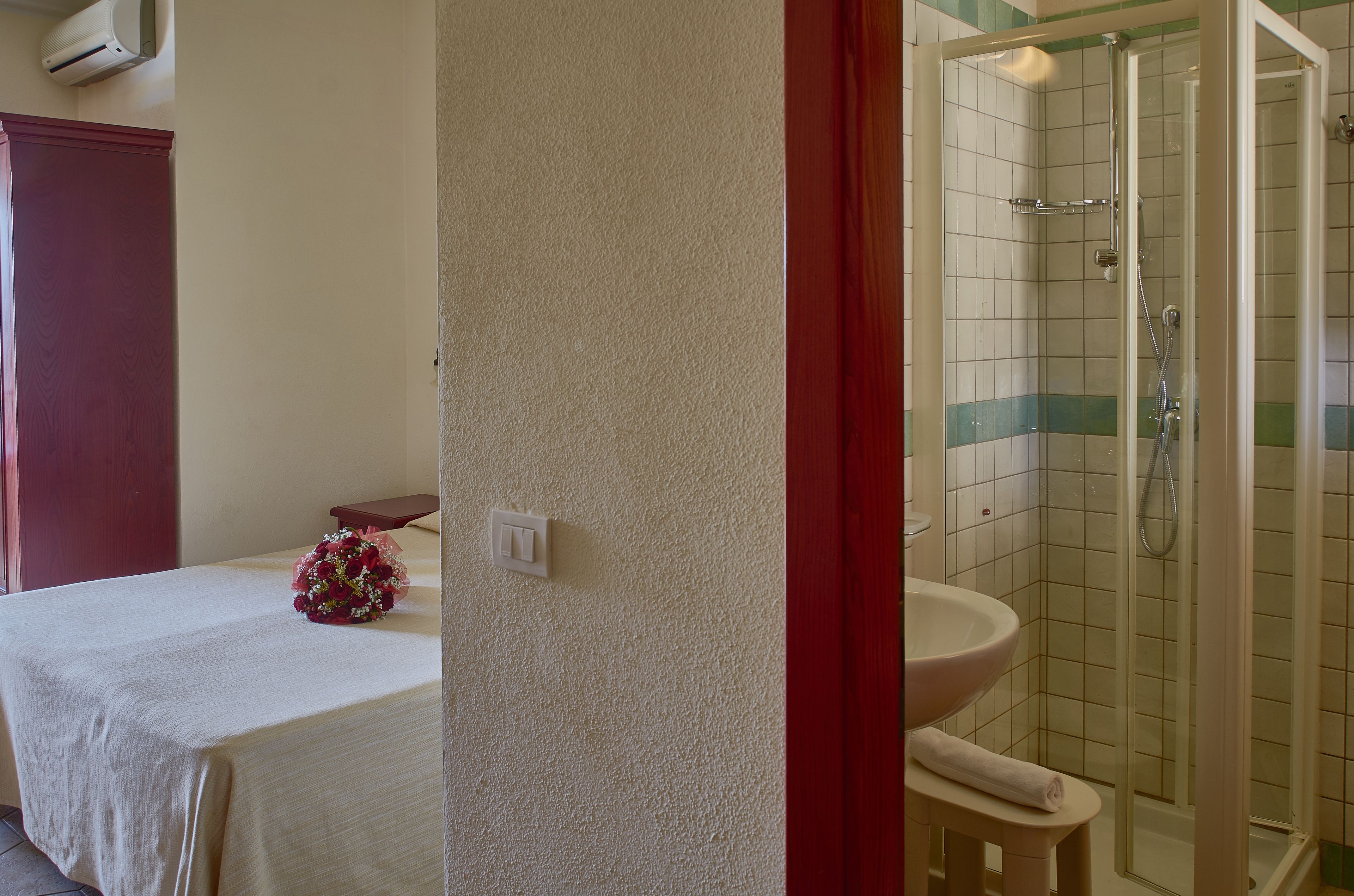 Un baño con ducha, lavamanos y una cama con mesita de noche y un ramo de flores.