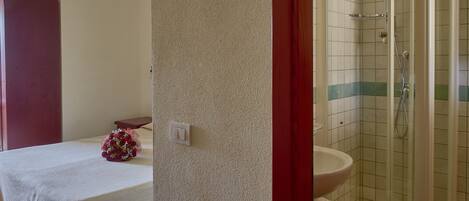 Un baño con ducha, lavamanos y una cama con mesita de noche y un ramo de flores.