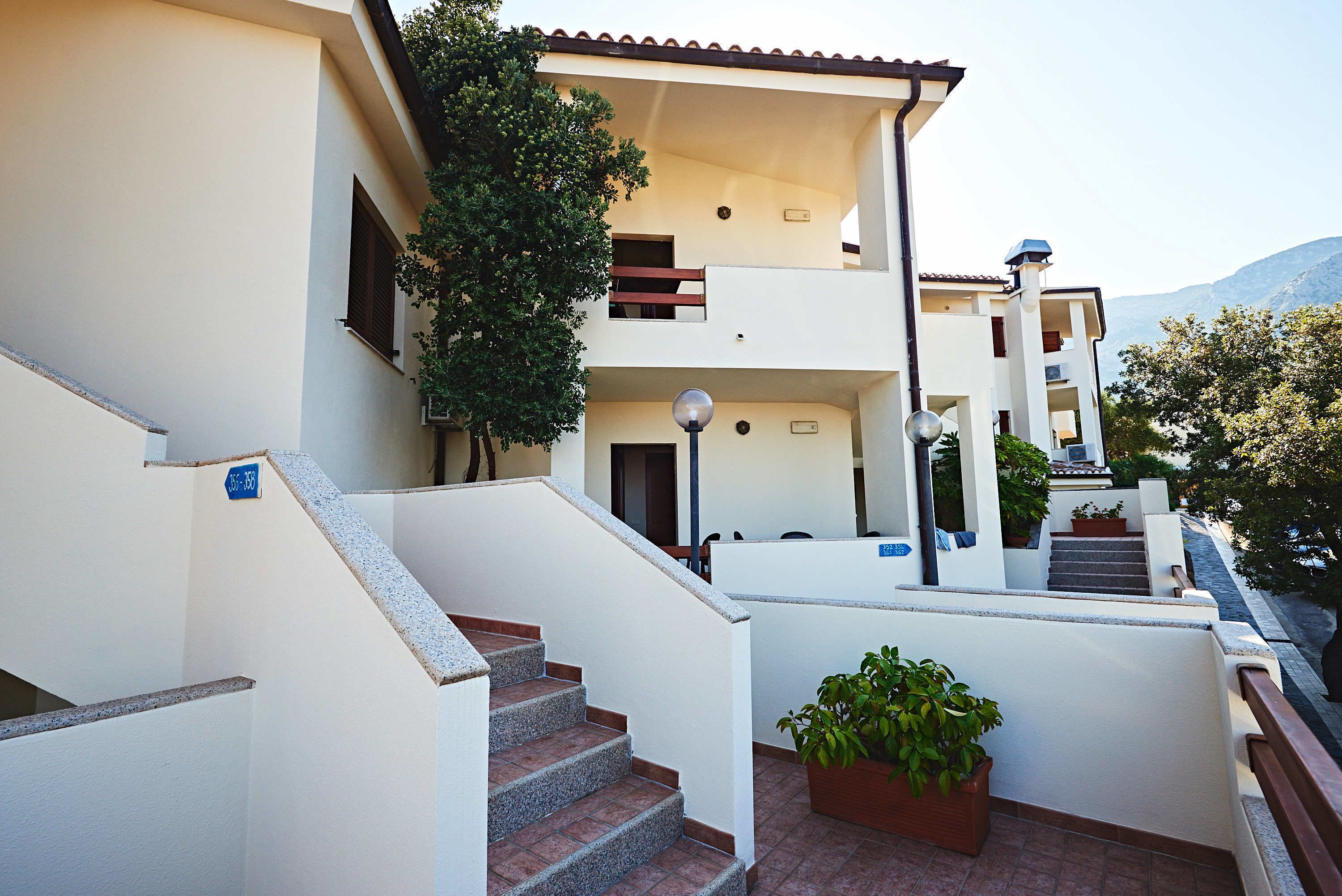A multi-level building with a staircase leading to a balcony, surrounded by potted plants and a clear view of the surrounding landscape.