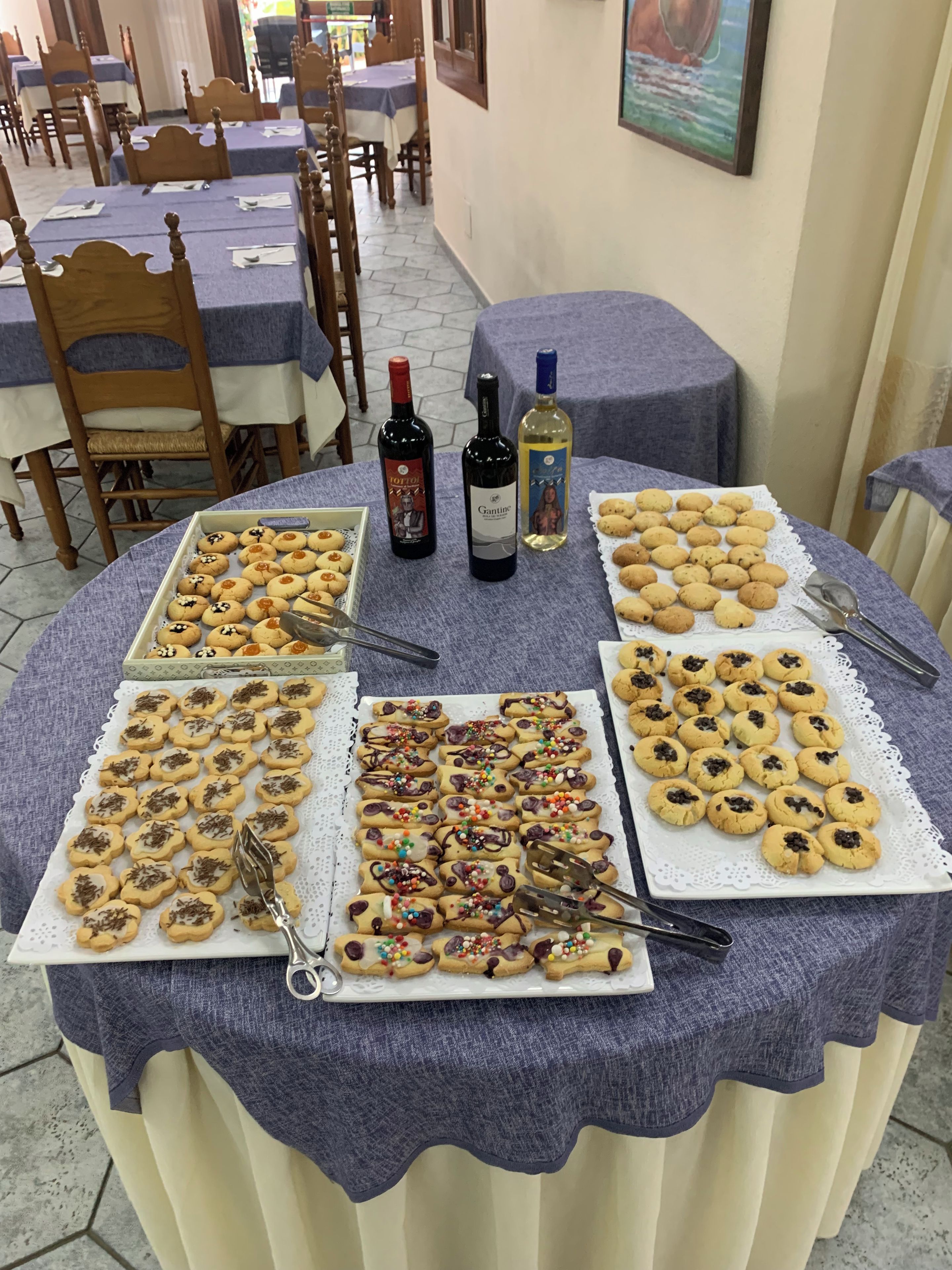 A table set with various cookies, two bottles of wine, and a plate of cookies on a tablecloth.