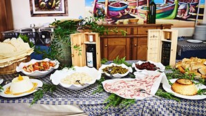 A table with various food items, including cheese, bread, and a painting of boats in the background.