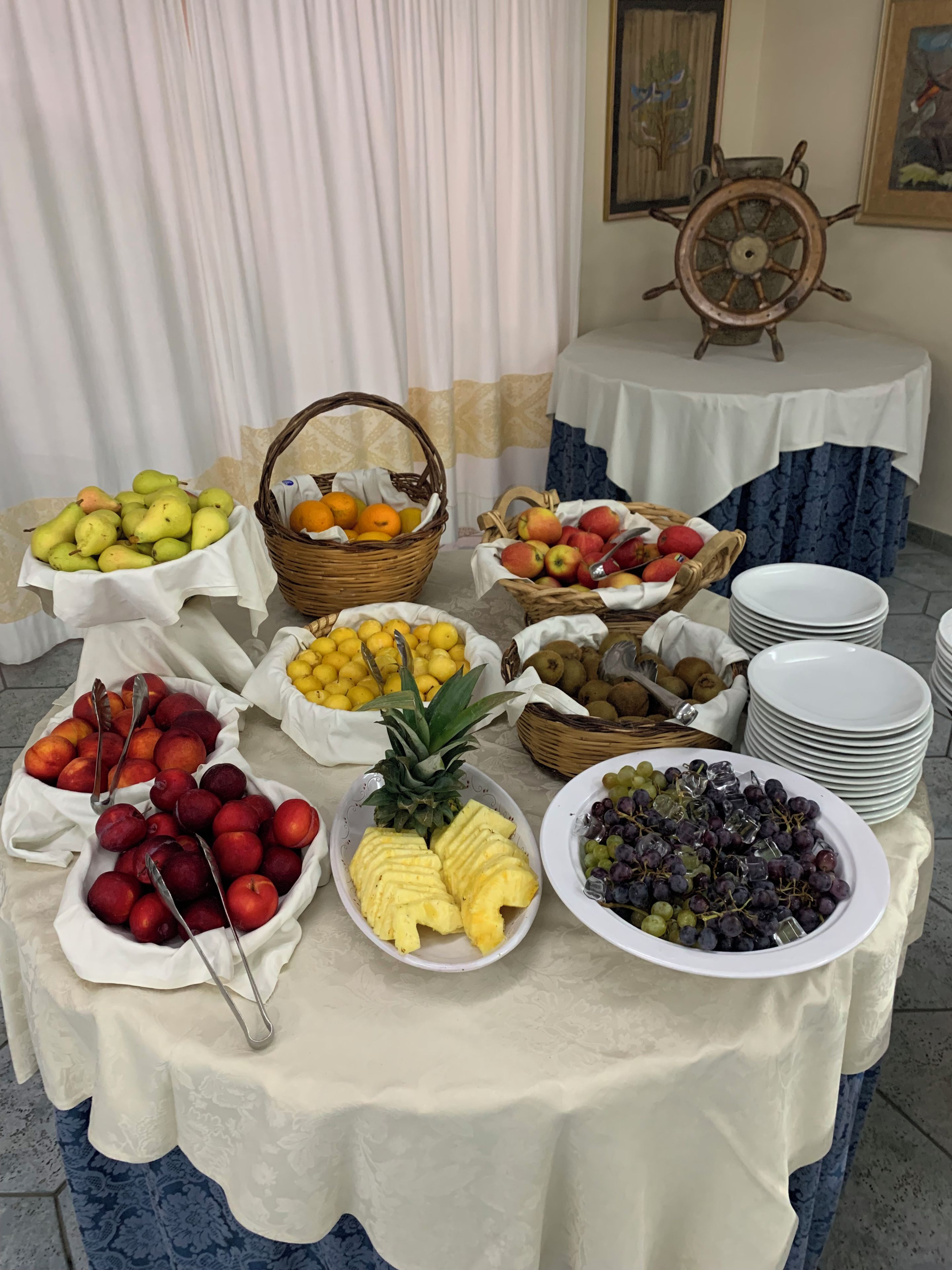 A buffet table with various fruits and a ship's wheel decoration.