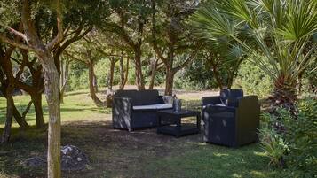 An outdoor seating area with wicker furniture and a small table, surrounded by trees and greenery.