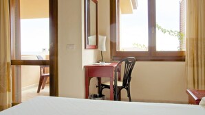 Habitació d'hotel amb llit, escriptori amb cadira, finestra i mirall.