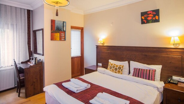 A hotel room with a large bed, a desk, a chair, a wooden headboard, and a painting on the wall. - Berce Hotel (Istanbul)