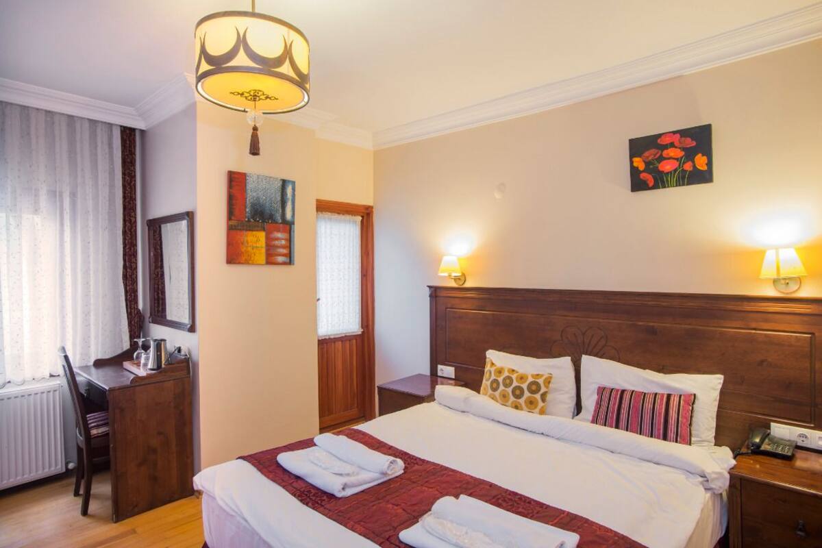 A hotel room with a large bed, a desk, a chair, a wooden headboard, and a painting on the wall.