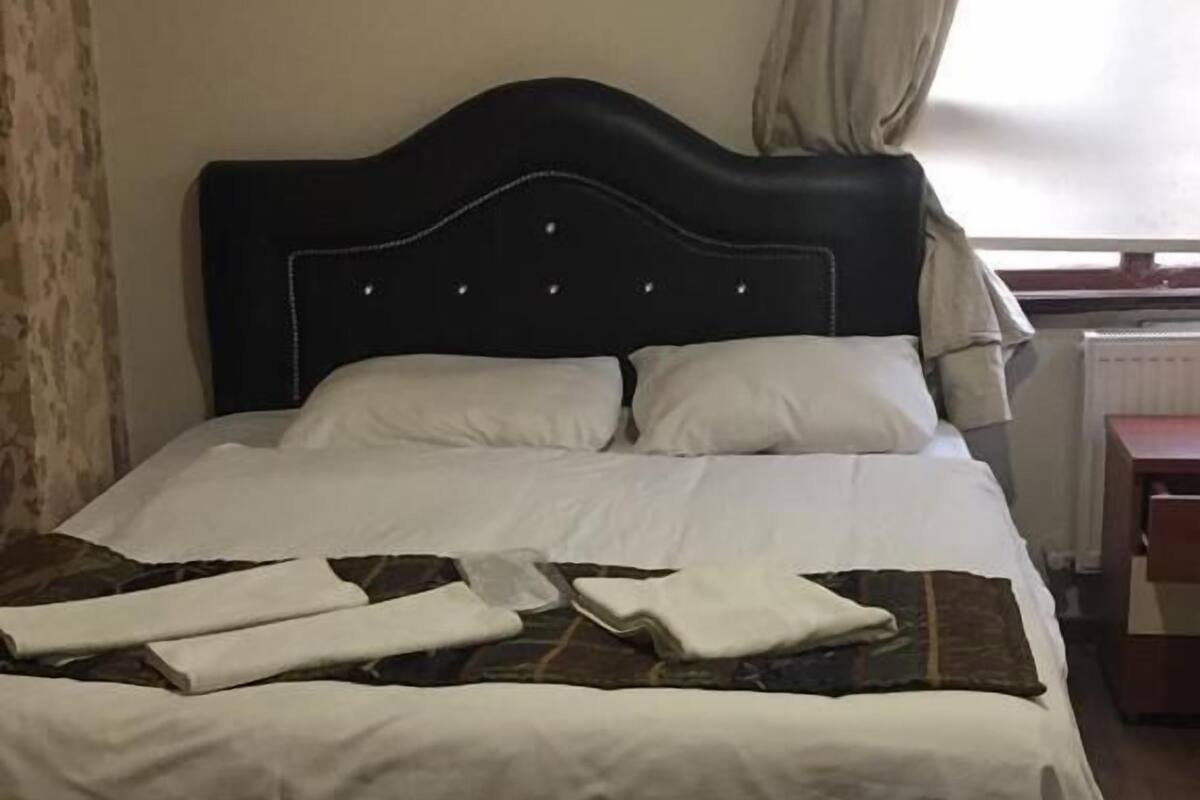 A bed with white bedding, a black headboard, and a painting of a red car and a boat on the wall.