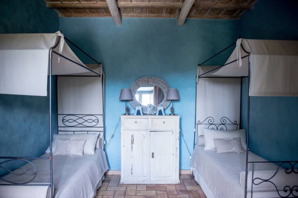 A room with two beds, a white wardrobe, a mirror, and a ceiling with exposed beams.
