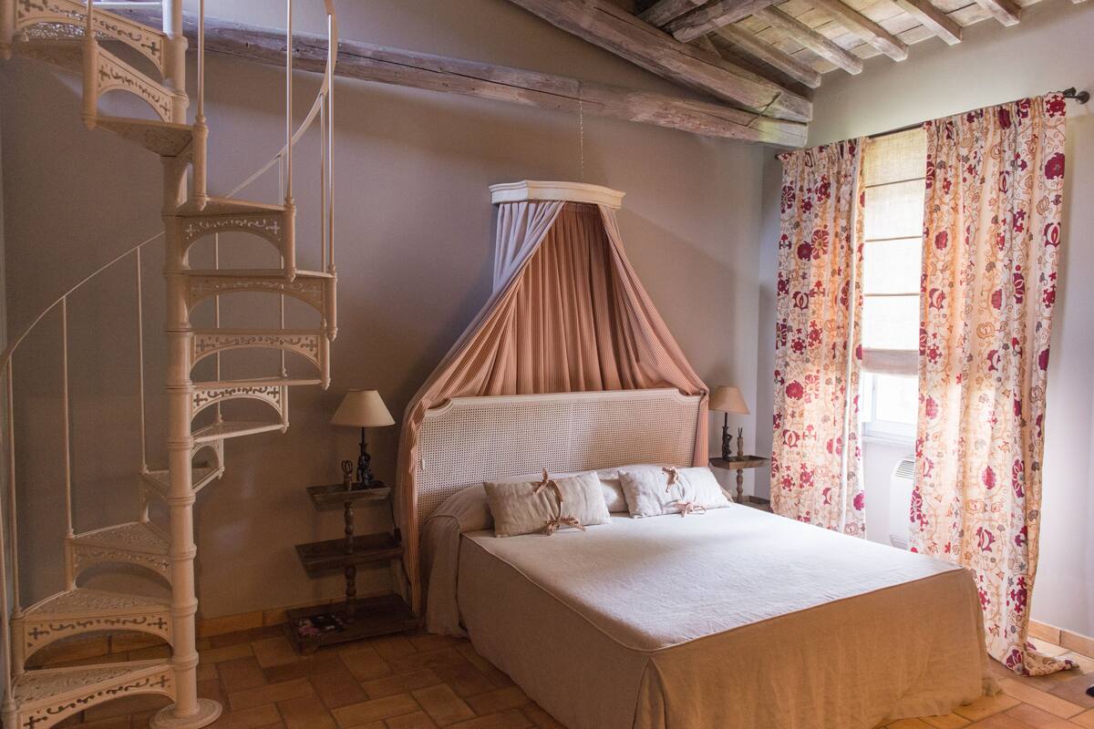A bedroom with a bed, a canopy, a wooden ladder, and a window with curtains.