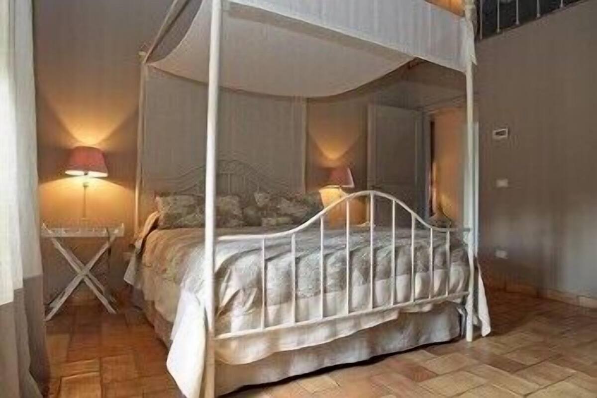 A four-poster canopy bed with a white metal frame, a small bedside table, and two lamps.