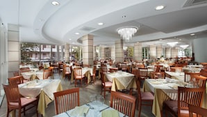 A spacious dining area with multiple tables and chairs, large windows, and a chandelier. - Michelangelo (Cesenatico)