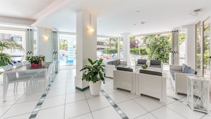 A modern hotel lobby with a dining area, seating arrangements, and large windows offering views of the outdoors. - Michelangelo (Cesenatico)
