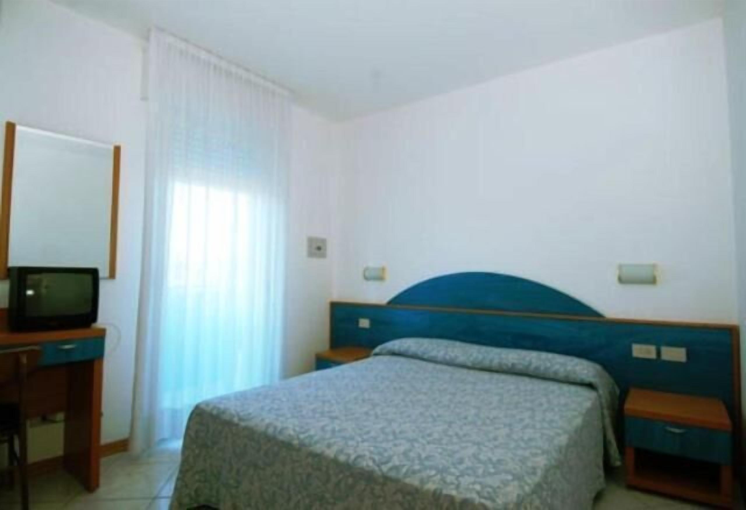 Une chambre d’hôtel avec un lit simple, un bureau avec une télévision et une fenêtre avec des rideaux.