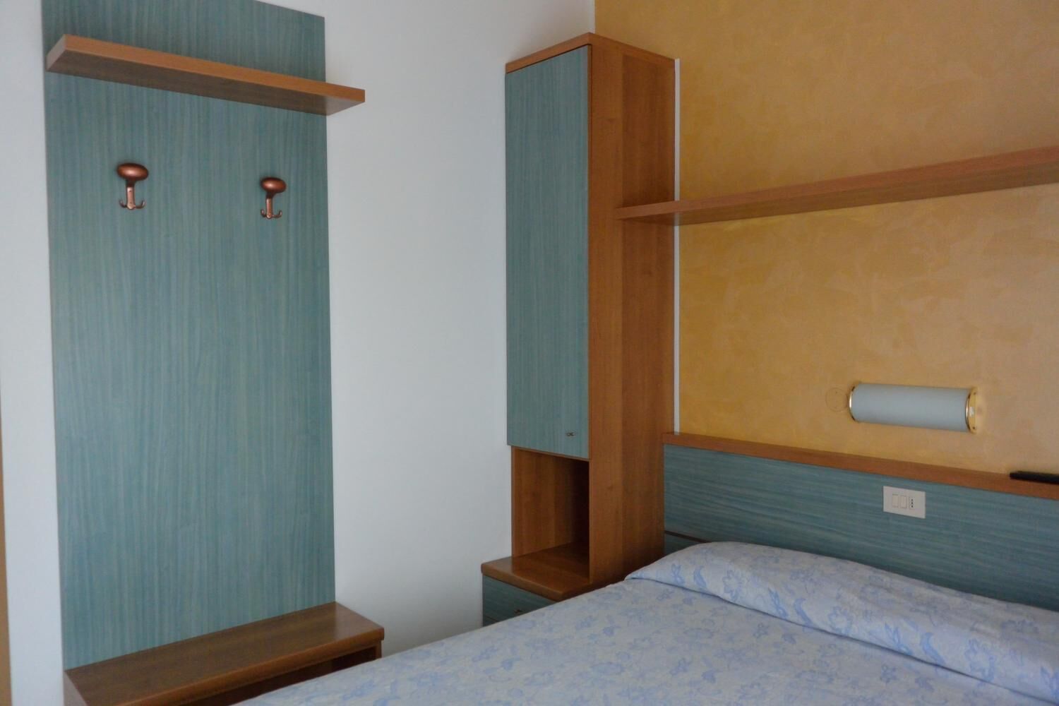 A bedroom with a bed, a wooden wardrobe, and a shelf unit.