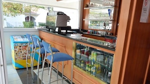 Un espace bar équipé d’une machine à café, d’une vitrine réfrigérée contenant des boissons et de tabourets de bar bleus.