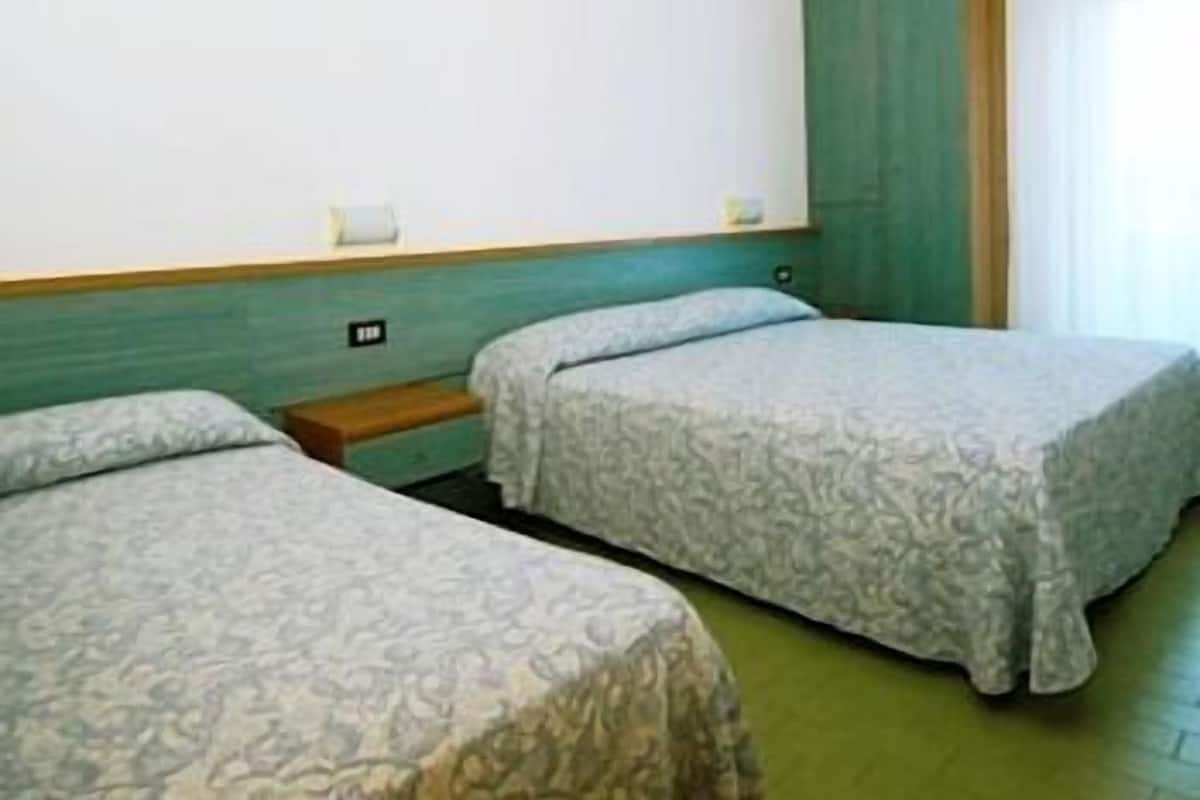 Ein Hotelzimmer mit zwei Betten, einer grünen Wand und einem Fenster mit Vorhängen.