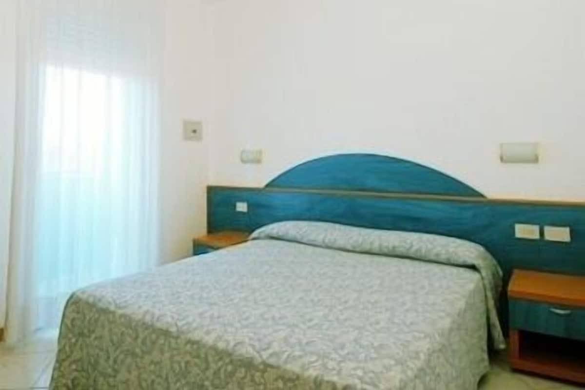 Ein Schlafzimmer mit einem Bett, Nachttischen und einem Fenster mit Vorhängen.