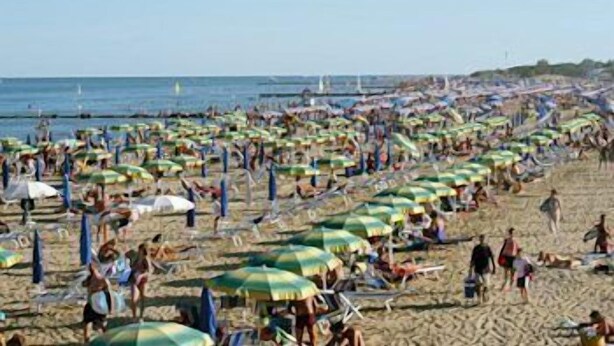 Une plage bondée, avec de nombreux parasols et beaucoup de monde.