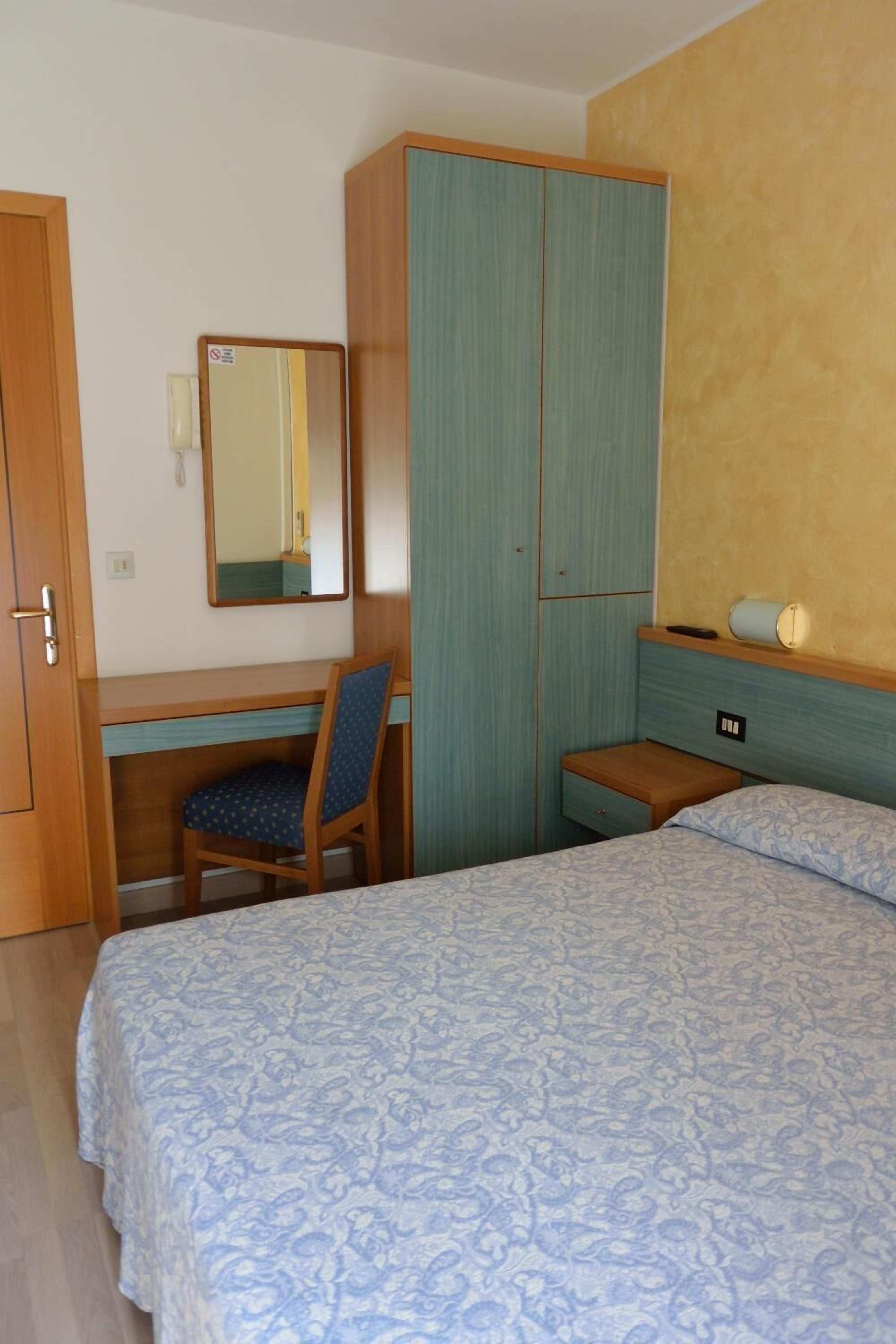 Ein Schlafzimmer mit Bett, Schreibtisch, Stuhl, Kleiderschrank und Spiegel.