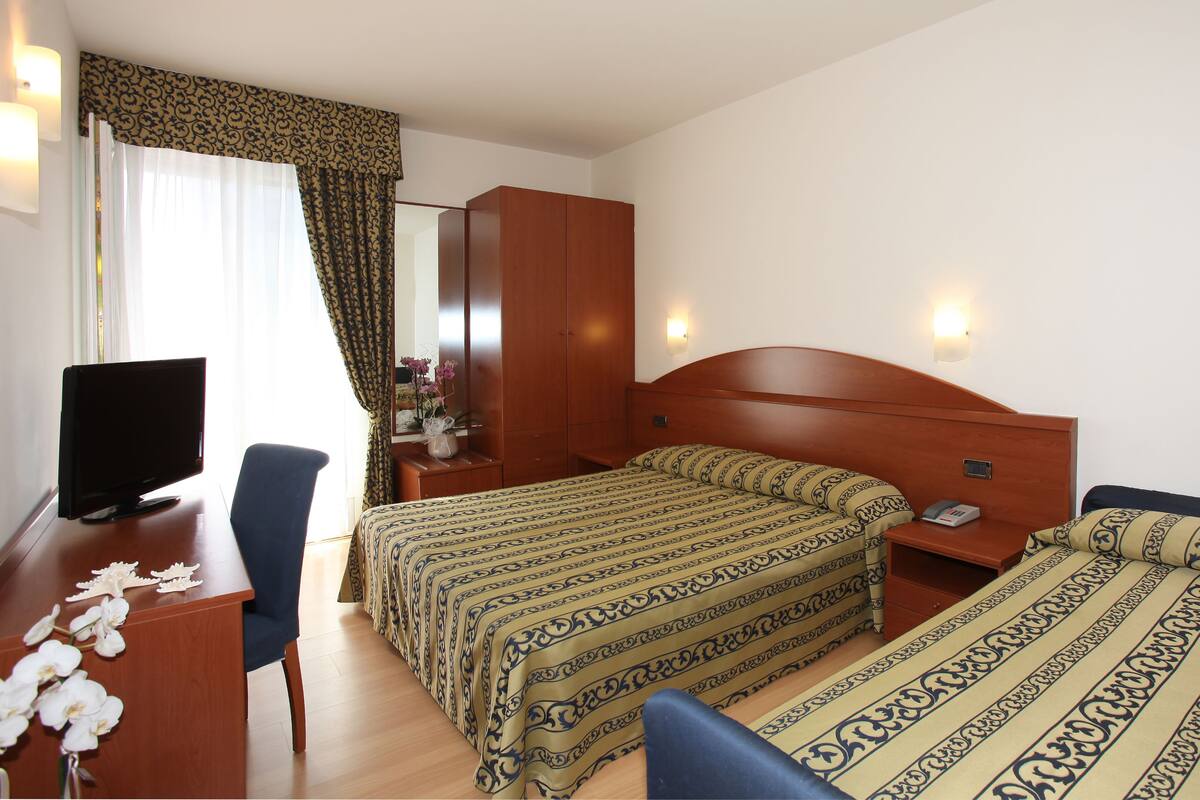A hotel room with two beds, a desk with a computer, a chair, and a mirror.