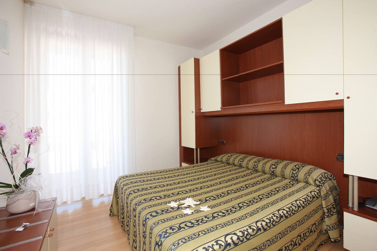 A bedroom with a bed, a nightstand, a dresser, and a window with curtains.