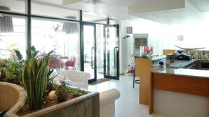 A modern kitchen with a central island, a dining area with a white sofa, and a large glass door leading to an outdoor space. - Hotel Santiago (Jesolo)